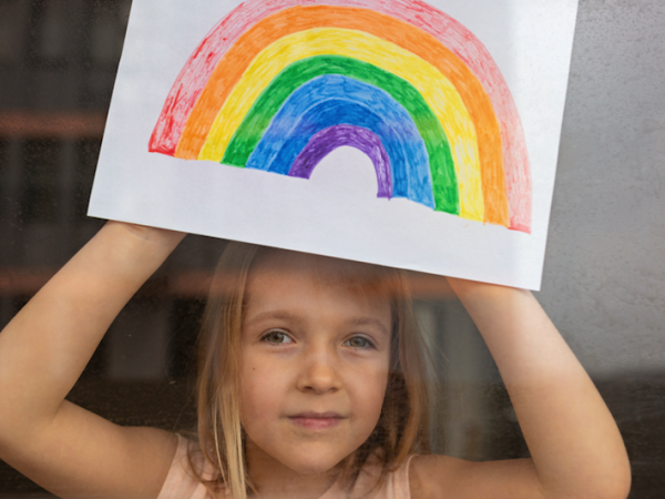 little girl showing rainbow drawing through the window
